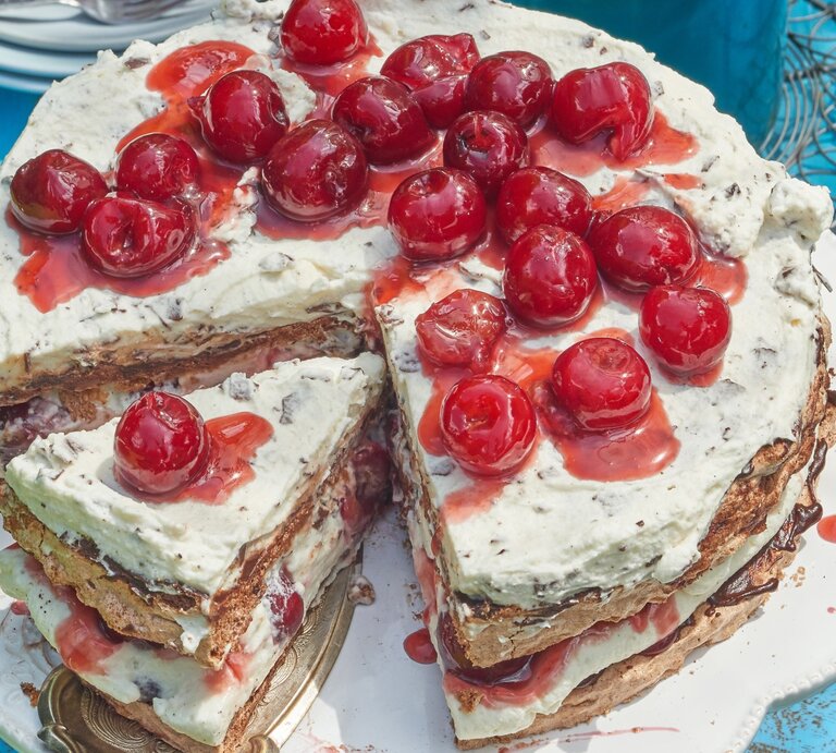 Angeschnittene Schwarzwälder Kirsch-Baisertorte mit Kirschen oben drauf auf blauem Untergrund.  | © Eat Club / Isabell Triemer 