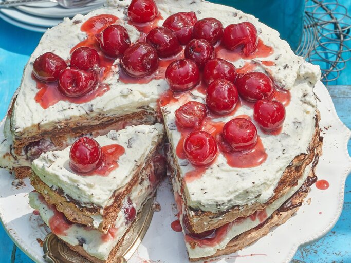 Angeschnittene Schwarzwälder Kirsch-Baisertorte mit Kirschen oben drauf auf blauem Untergrund.  | © Eat Club / Isabell Triemer 
