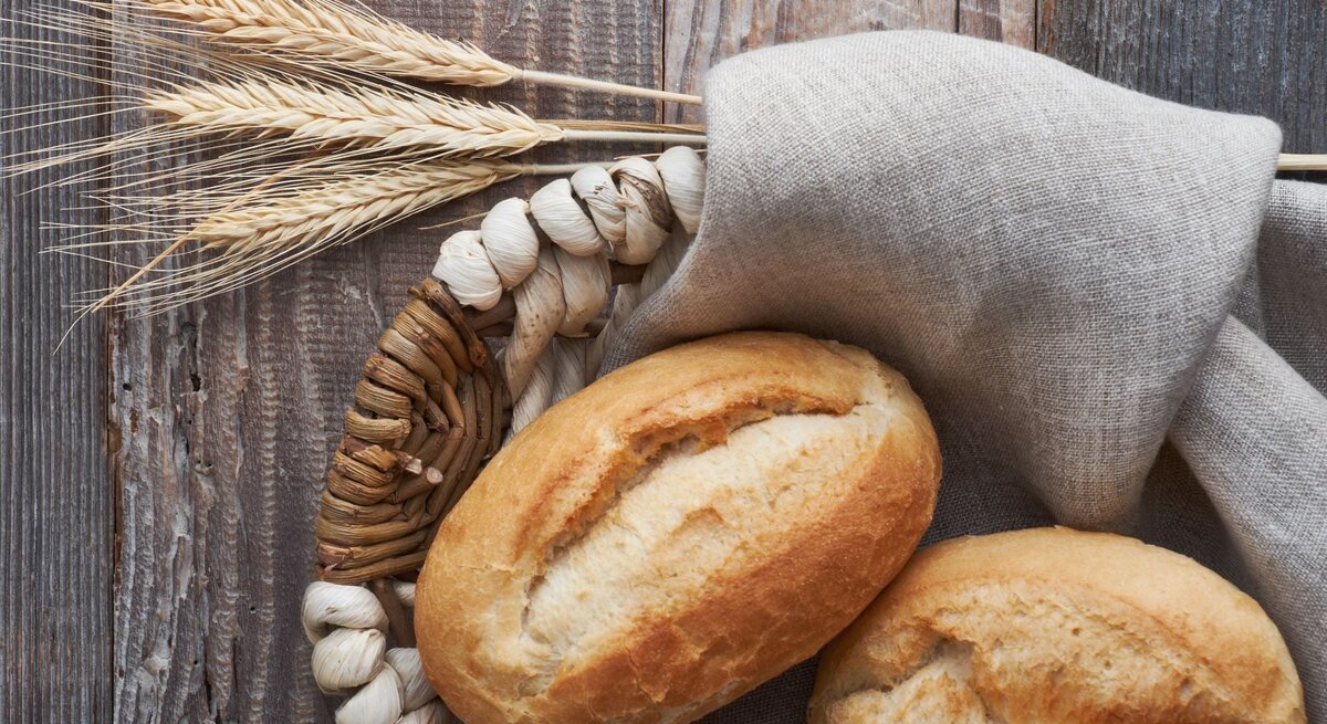 Zwei Brötchen im Brotkorb auf graubraunem Holz. 
