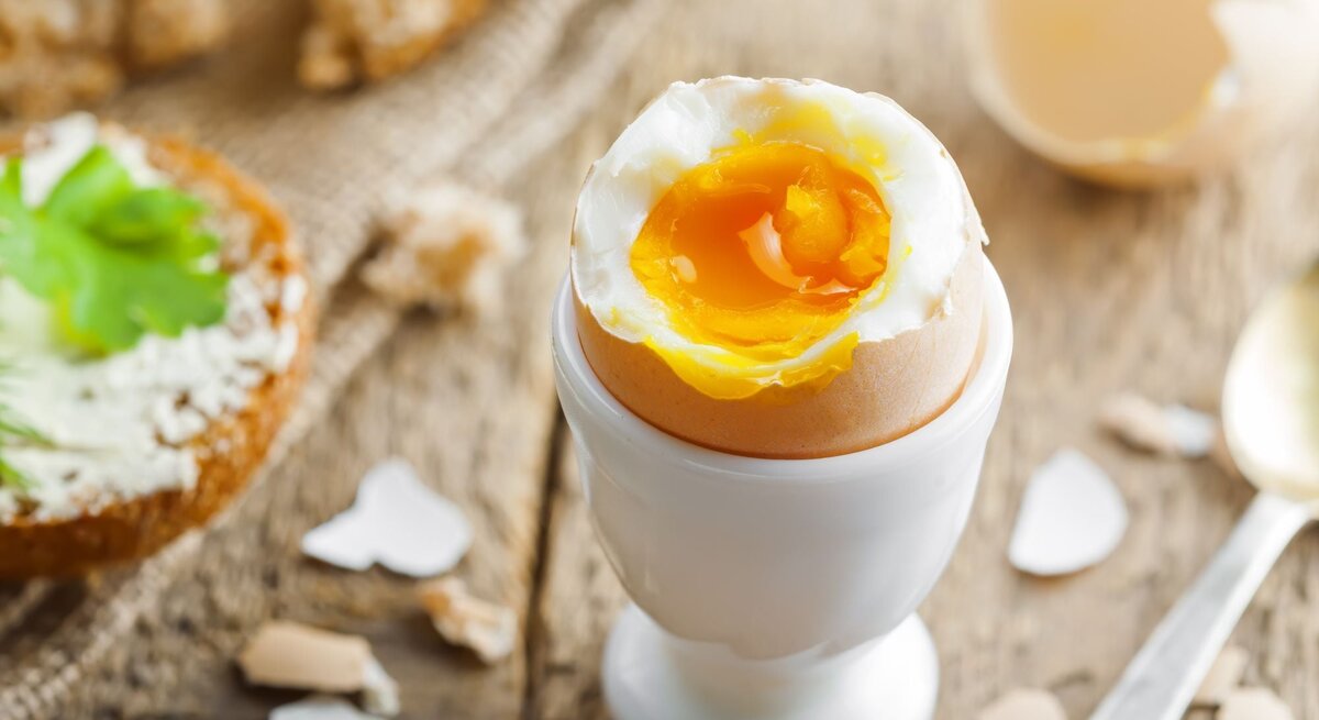 Wachsweich gekochtes Ei in einem weißen Eierbecher auf Holztisch. 