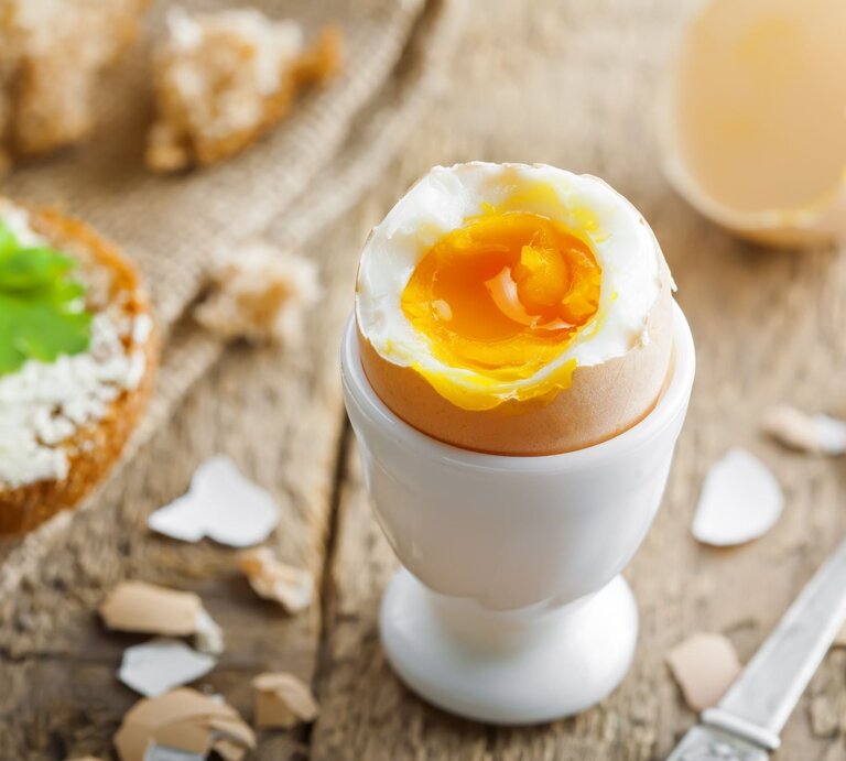 Wachsweich gekochtes Ei in einem weißen Eierbecher auf Holztisch.  | © AdobeStock/Maxim Khytra
