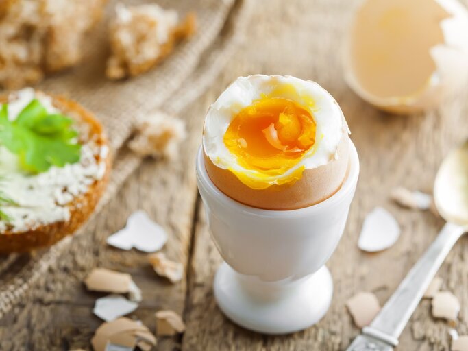 Wachsweich gekochtes Ei in einem weißen Eierbecher auf Holztisch.  | © AdobeStock/Maxim Khytra