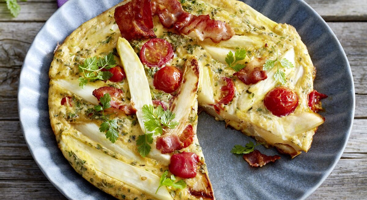 Spargel-Frittata auf einem blauen Teller auf hölzernem Hintergrund. 