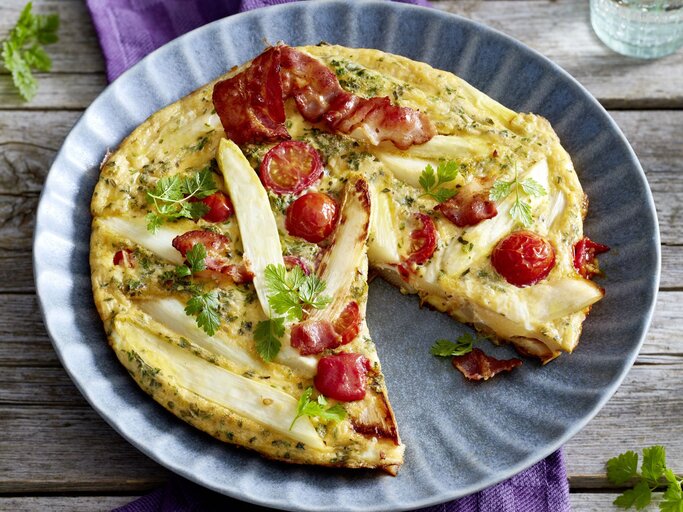 Spargel-Frittata auf einem blauen Teller auf hölzernem Hintergrund.  | © EAT CLUB/Isabell Triemer