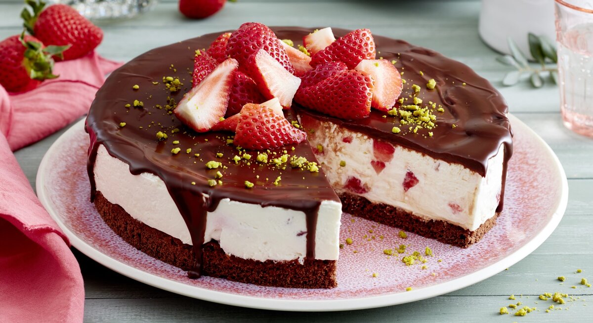Joghurt-Erdbeer-Torte auf einem rosa Teller auf hellgrünem Hintergrund. Rechts Geschirr und links rosa Geschirrtuch. 