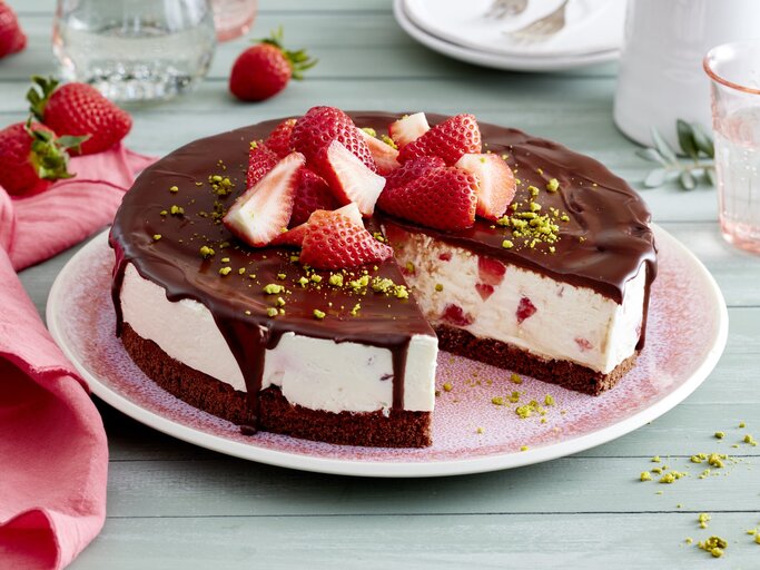 Joghurt-Erdbeer-Torte auf einem rosa Teller auf hellgrünem Hintergrund. Rechts Geschirr und links rosa Geschirrtuch.  | © EAT CLUB/Isabell Triemer