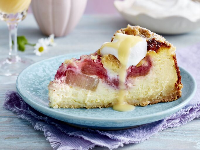 Rhabarber-Käsekuchen auf einem blauen Hintergrund. Hinten Gläser und Gänseblümchen verteilt. | © EAT CLUB/Isabell Triemer