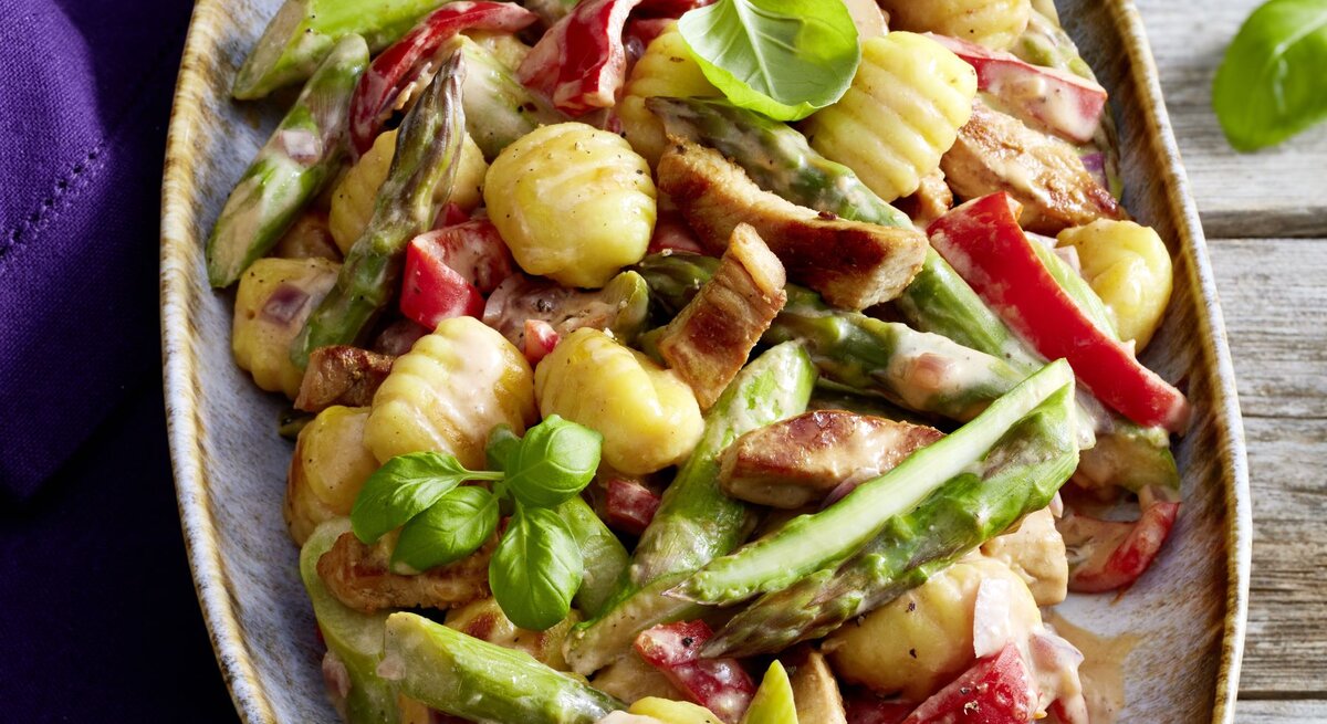 Gnocchi-Schnitzel-Pfanne auf einem großen Teller auf hölzernem Hintergrund. Links davon ein blaues Geschirrtuch.