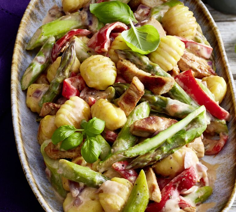 Gnocchi-Schnitzel-Pfanne auf einem großen Teller auf hölzernem Hintergrund. Links davon ein blaues Geschirrtuch. | © EAT CLUB/Isabell Triemer