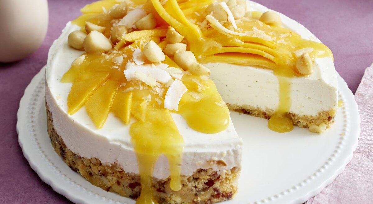 Macadamia-Kokos-Cheesecake auf einem Tortenteller auf rosa Hintergrund.