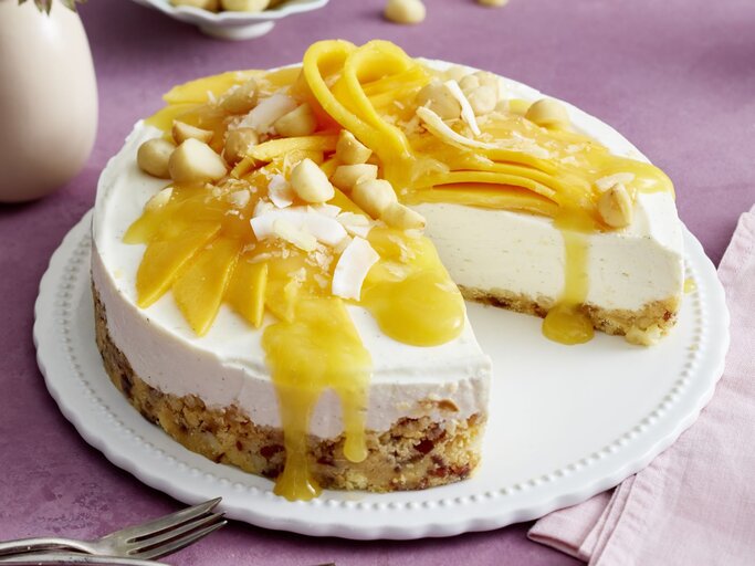 Macadamia-Kokos-Cheesecake auf einem Tortenteller auf rosa Hintergrund. | © EAT CLUB/Isabell Triemer