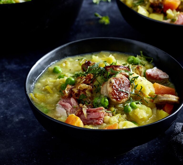Erbsenduo mit Rostbratwursttalern in einer schwarzen Schüssel auf dunklem Hintergrund. | © EAT CLUB/Isabell Triemer