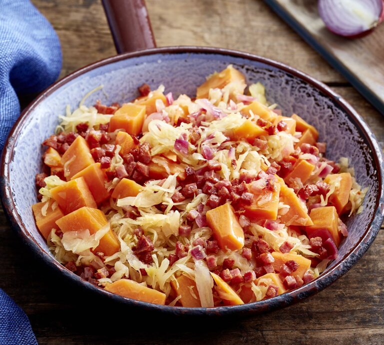 Süßkartoffel-Sauerkraut-Pfanne auf hölzernem Hintergrund. Links davon ein blaues Geschirrtuch. | © EAT CLUB/Isabell Triemer