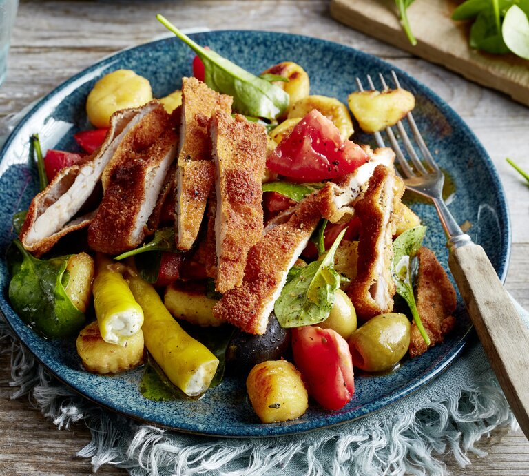 Antipasti-Schnitzel-Salat auf einem blauen Teller auf einem hellblauen Geschirrtuch auf hölzernem Hintergrund. | © EAT CLUB / Isabell Triemer
