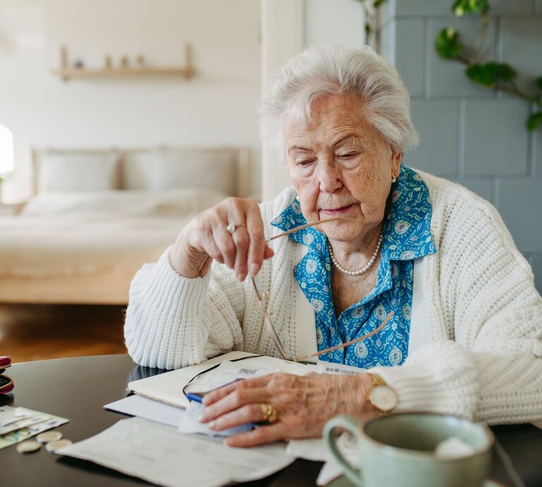 Frau sitzt am Tisch und guckt auf Rechnungen. | © gettyimages/	Halfpoint Images