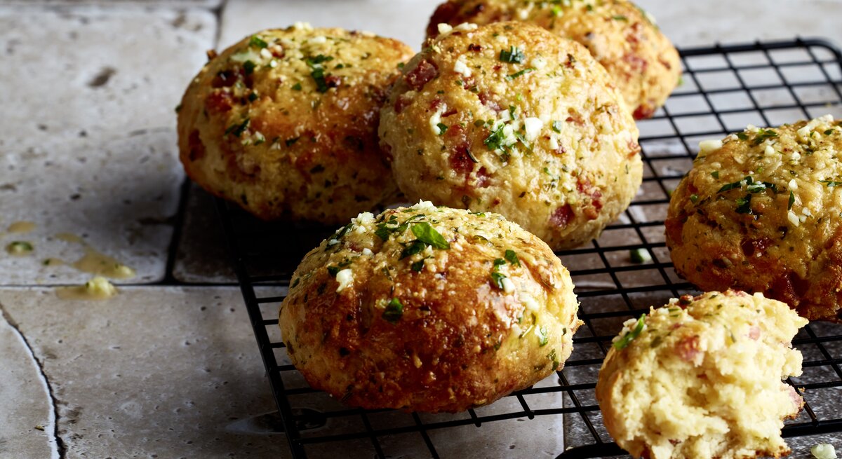 Triple-Cheese-Brötchen aus der Pfanne auf einem schwarzen Gitter auf grauem Hintergrund. 