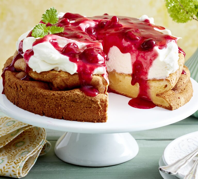 Rote-Grütze-Torte mit Puddingboden auf einem weißen Tortenteller auf grünem Hintergrund. | © EAT CLUB/Isabell Triemer