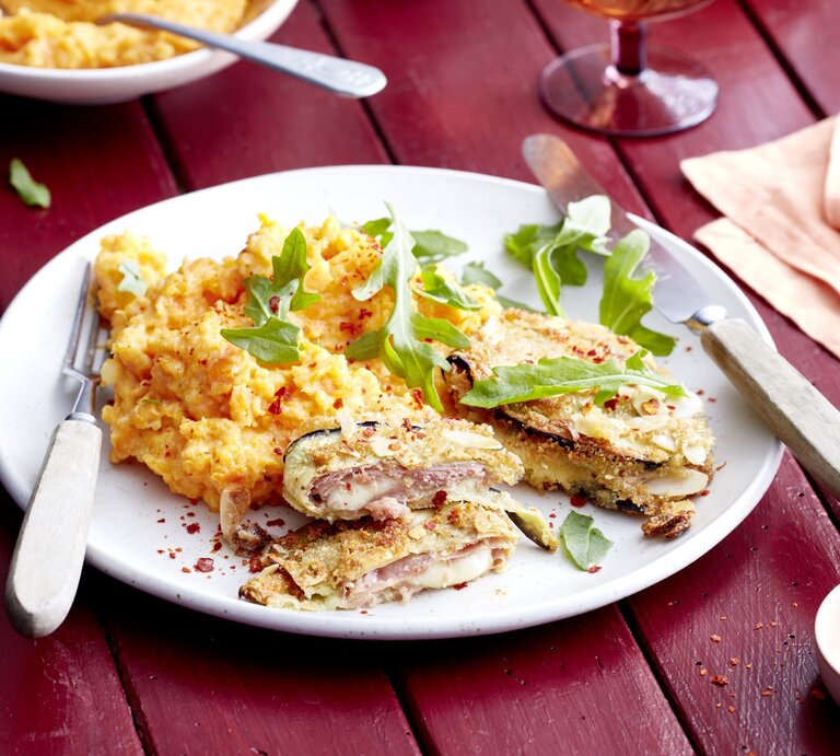 Auberginen-Cordon-Bleu auf einem weißen Teller auf dunkelrotem Hintergrund. | © EAT CLUB/Isabell Triemer