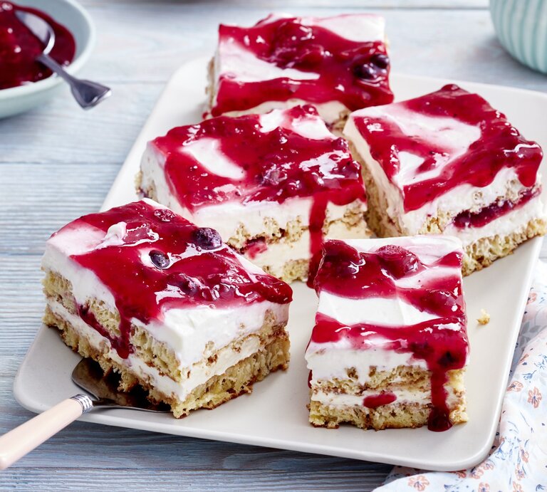 Rote-Grütze-Tiramisu-Schnitten auf einem weißen Teller auf grauem Hintergrund. Links oben eine Schüssel mit Roter Grütze. | © EAT CLUB/Isabell Triemer