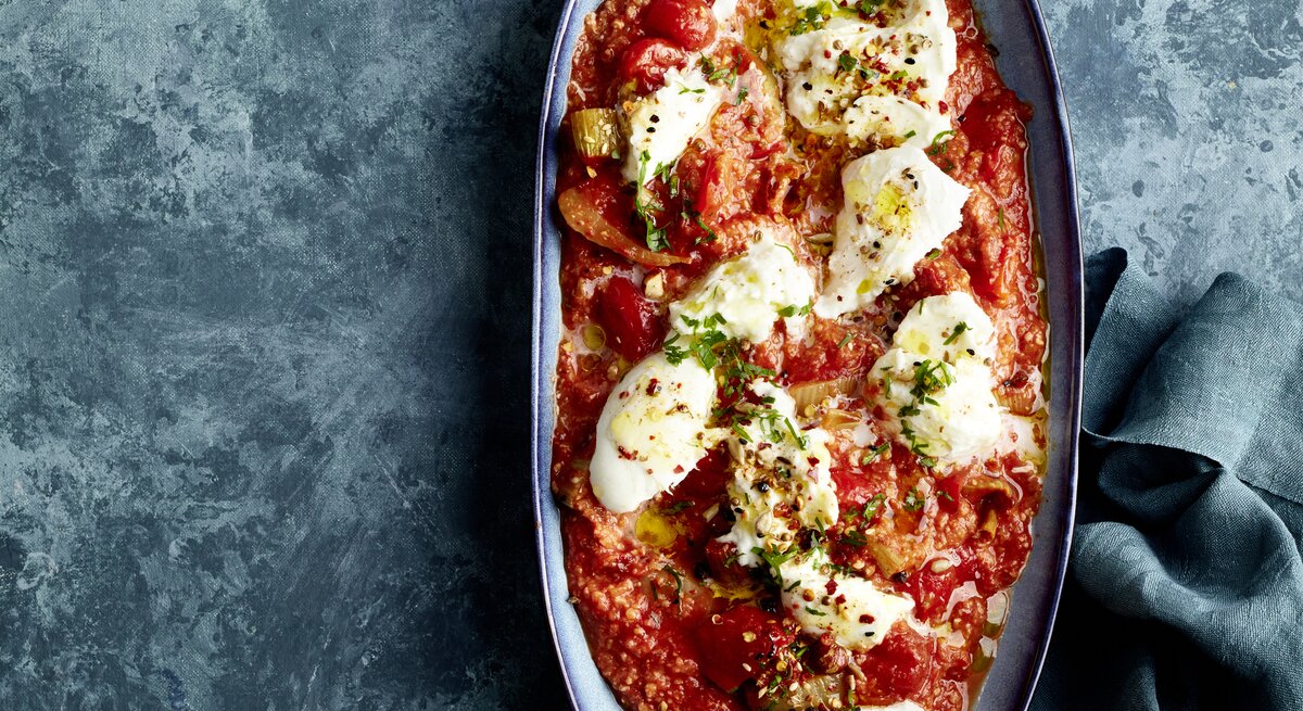 Zerzupfter Büffelmozzarella auf Röstgemüse à la Romesco in einer Auflaufform auf dunklem Hintergrund.
