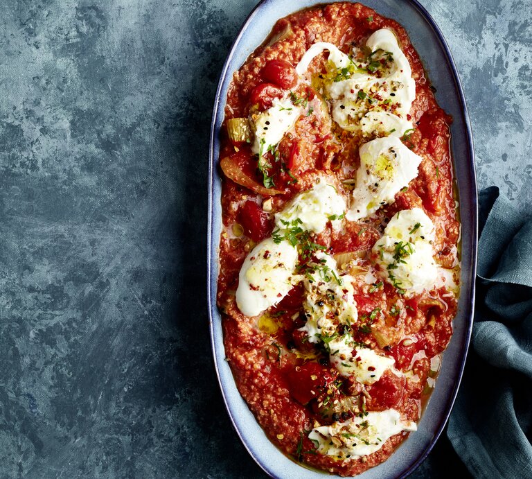 Zerzupfter Büffelmozzarella auf Röstgemüse à la Romesco in einer Auflaufform auf dunklem Hintergrund. | © EAT CLUB/Isabell Triemer