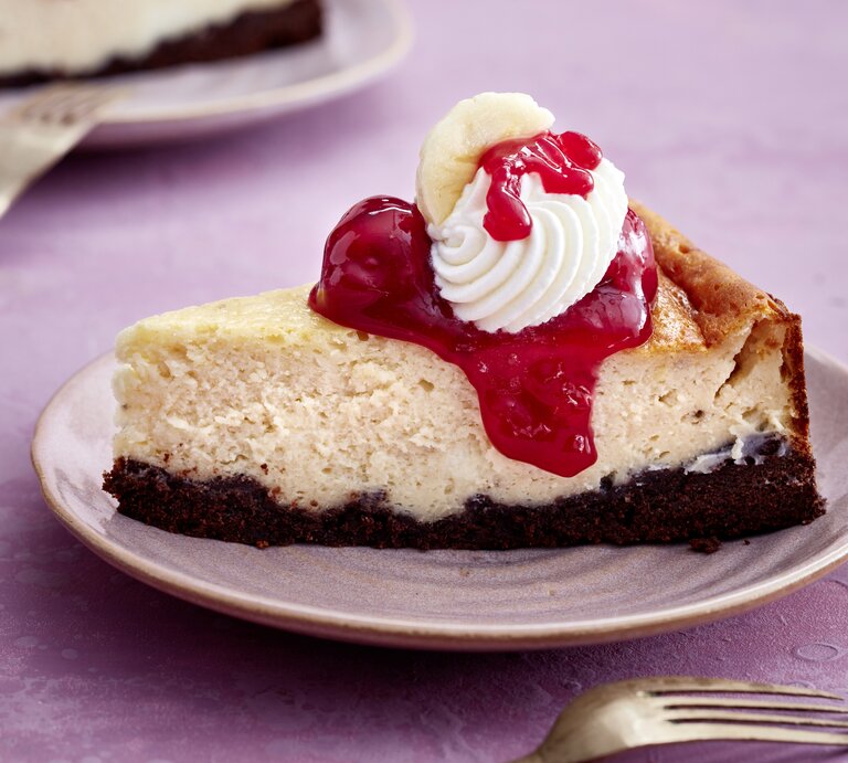 Ein Stück KiBa-Cheesecake auf einem Teller auf rosa Hintergrund. Vorne auf dem Foto eine Gabel. | © EAT CLUB/Isabell Triemer