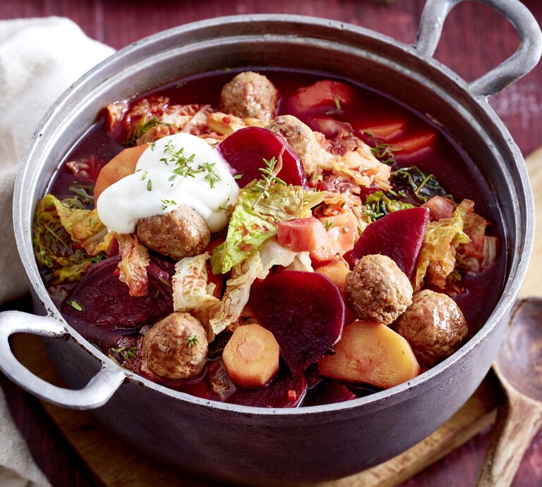Rote-Bete-Topf mit Hackbällchen in einem schwarzen Topf auf hölzernem Hintergrund.  | © EAT CLUB/Isabell Triemer