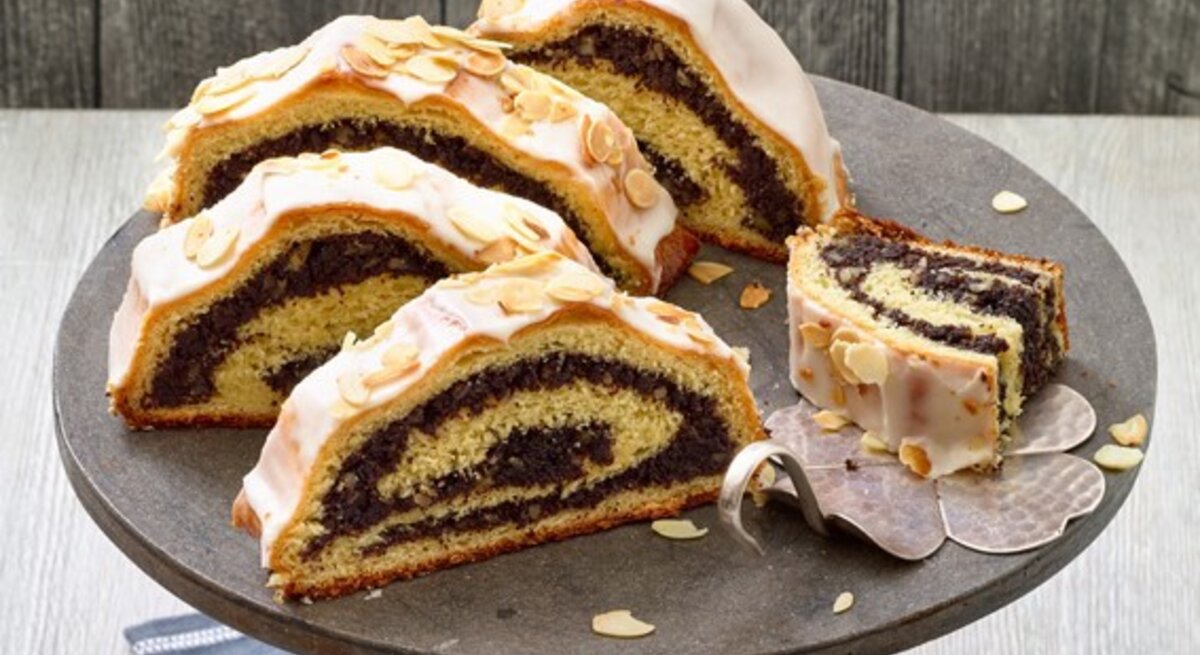 Mohnstollen auf einem schwarzen Tortenteller auf hölzernem Hintergrund. 