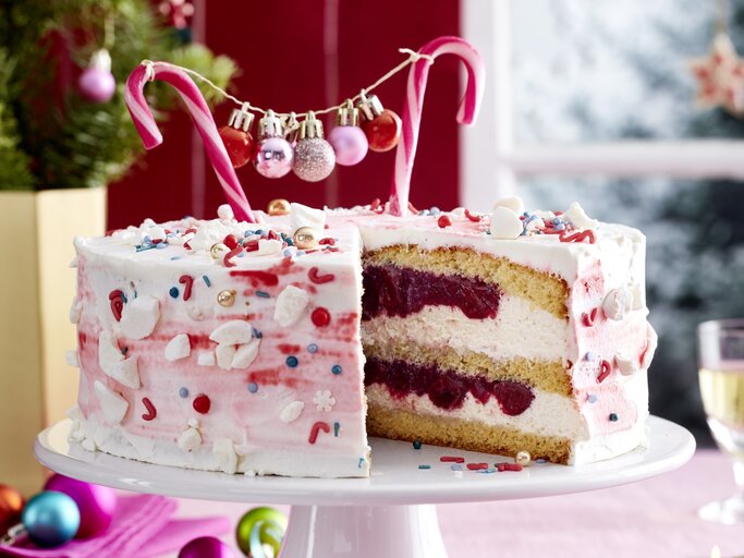 Zuckerstangen-Torte auf einem weißen Tortenteller auf einer rosa Tischdecke dekoriert mit kleinen Weihnachtskugeln. Links hinten auf dem Foto ein kleiner Tannenbaum. | © EAT CLUB / Isabell Triemer