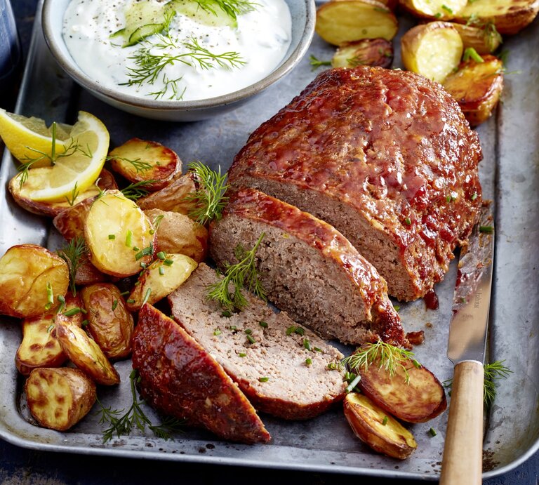 Glasierter Hackbraten mit Kartoffeln auf einem silbernen Blech. Oben auf dem Foto ein Schüsselchen mit einer Soße, rechts unten ein Messer.  | © EAT CLUB/Isabell Triemer