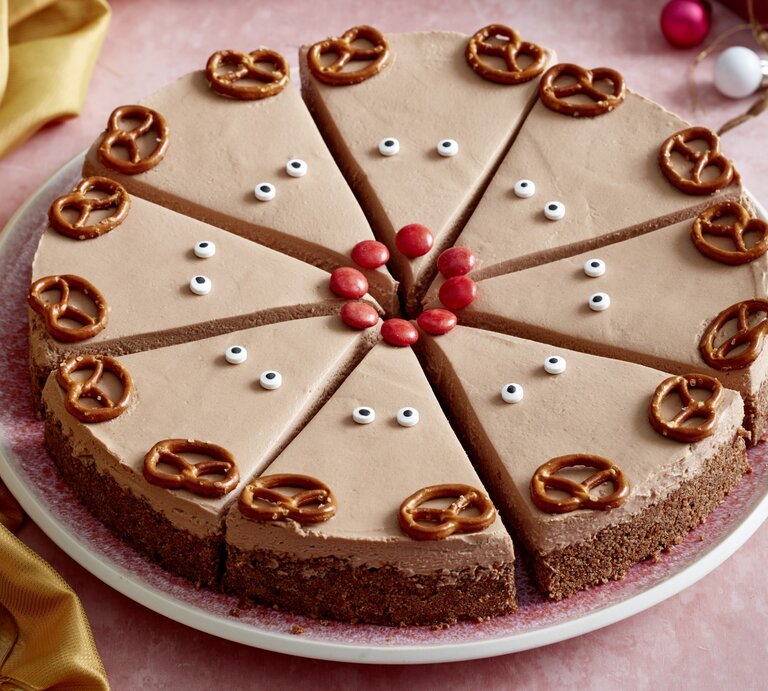 Rudolph-Cheesecake auf einem rosa Teller auf rosa Hintergrund. Links ein gelbes Tuch und rechts Weihnachtskugeln verteilt. | © EAT CLUB/Isabell Triemer