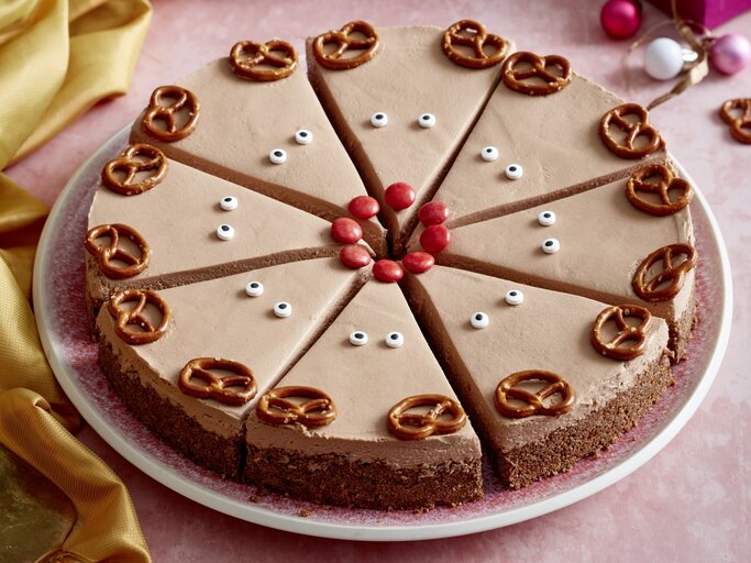 Rudolph-Cheesecake auf einem rosa Teller auf rosa Hintergrund. Links ein gelbes Tuch und rechts Weihnachtskugeln verteilt. | © EAT CLUB/Isabell Triemer