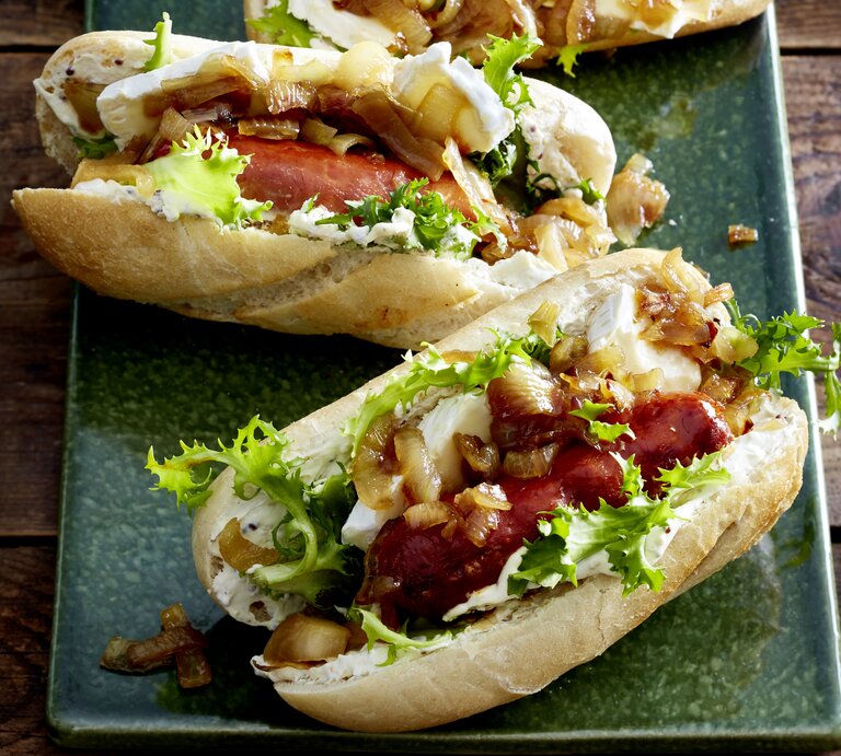 zwei Hotdogs gefüllt mit Camembert und schwarfen Würsten auf grünem Teller. | © EAT CLUB/Isabell Triemer