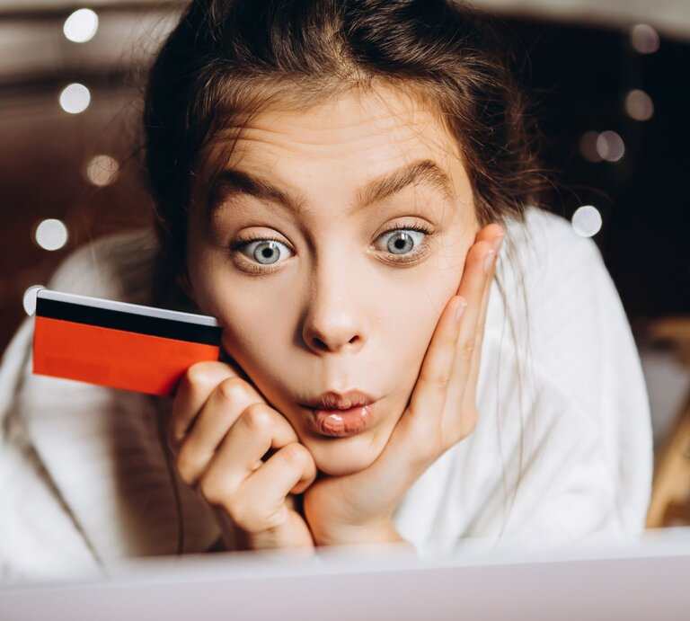 Eine Frau guckt entsetzt auf ihren Laptop und erkennt die Kostenfallen. Mit Kreditkarte in der Hand. | © gettyimages/	Yuliia Lisiana / 500px