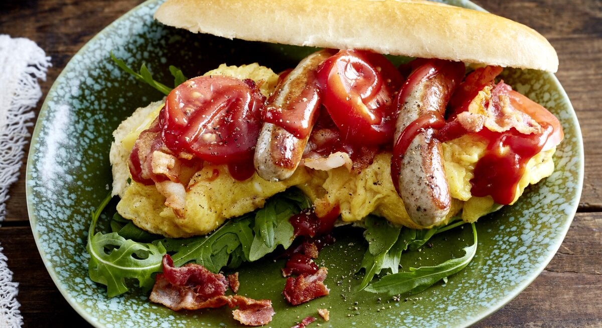 Hotdog mit Bacon & Rührei auf einem grauen Teller auf hölzernem Hintergrund. 