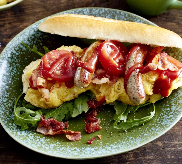 Hotdog mit Bacon & Rührei auf einem grauen Teller auf hölzernem Hintergrund.  | © EAT CLUB/Isabell Triemer