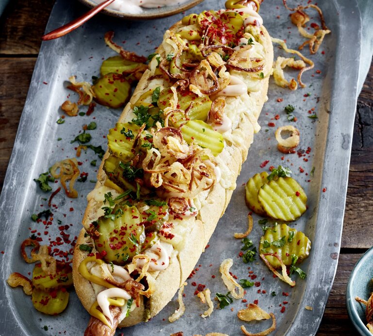 Hotdog ofengebacken im Kräuterbaguette auf einem silberfarbenen Blech auf hölzernem Hintergrund.  | © EAT CLUB/Isabell Triemer