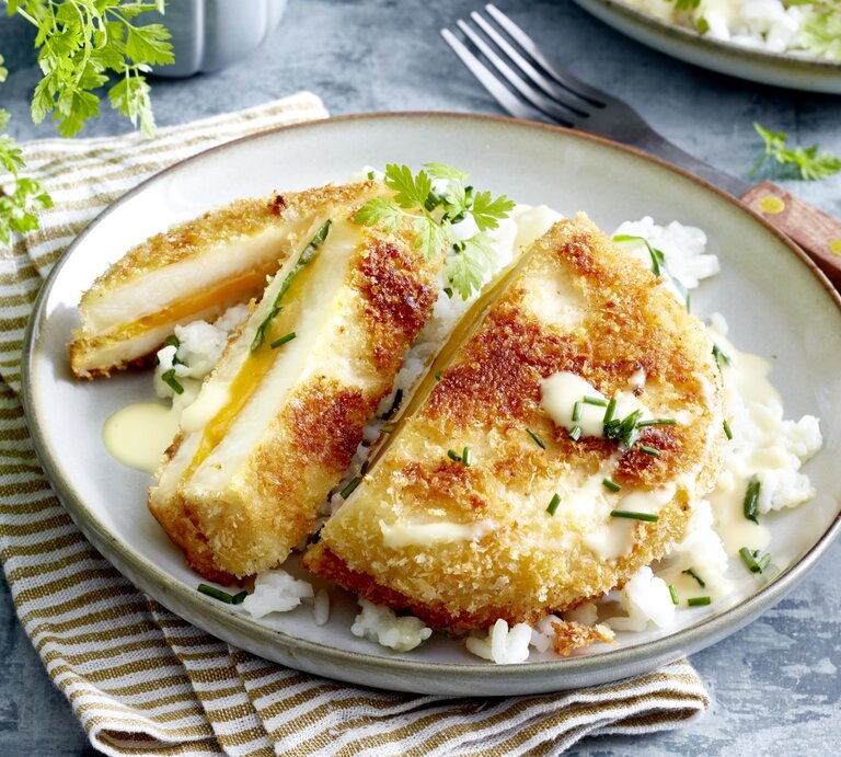 Sellerie-Cordon-bleu auf einem grauen Teller auf einem braun-weiß-gestreiften Geschirrtuch. Der Hintergrund ist grau und rechts von dem Teller liegt eine Gabel.  | © EAT CLUB / Isabell Triemer