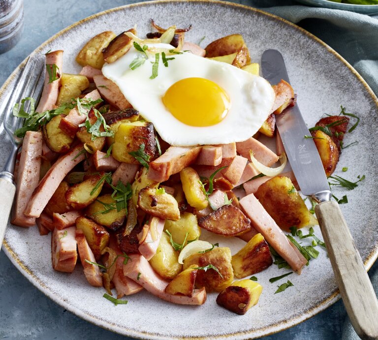 Bratkartoffeln auf bayerische Art auf einem weißen Teller, links und rechts Besteck. Der Hintergrund ist grau. | © EAT CLUB / Isabell Triemer