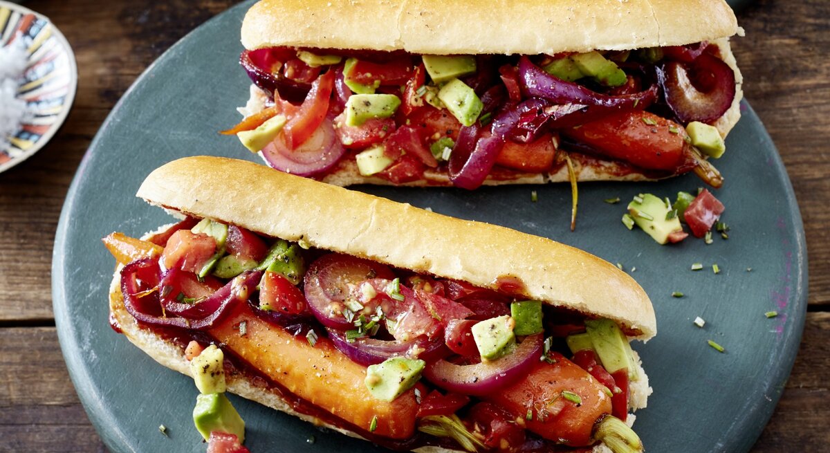 Hotdog mit Möhren und Salsa auf einem dunkelgrauen Teller auf hölzernem Hintergrund.