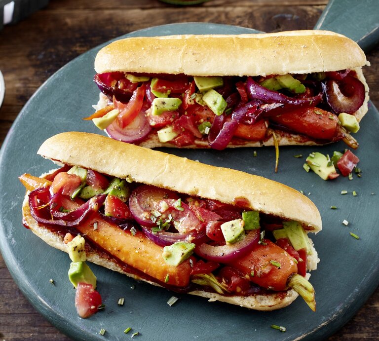 Hotdog mit Möhren und Salsa auf einem dunkelgrauen Teller auf hölzernem Hintergrund. | © EAT CLUB / Isabell Triemer