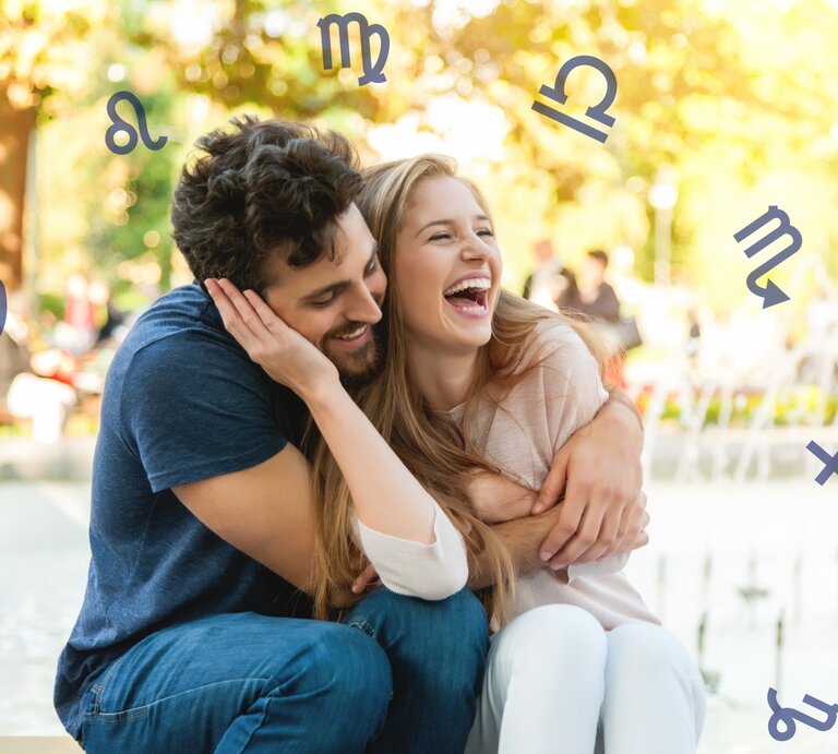 Ein glückliches Paar sitzt Arm in Arm in der Natur und ist umgeben vom Tierkreis und den astrologischen Symbolen der Tierkreiszeichen. | © Getty Images Pro/ stock-eye und Chikovnaya via Canva.com [M]