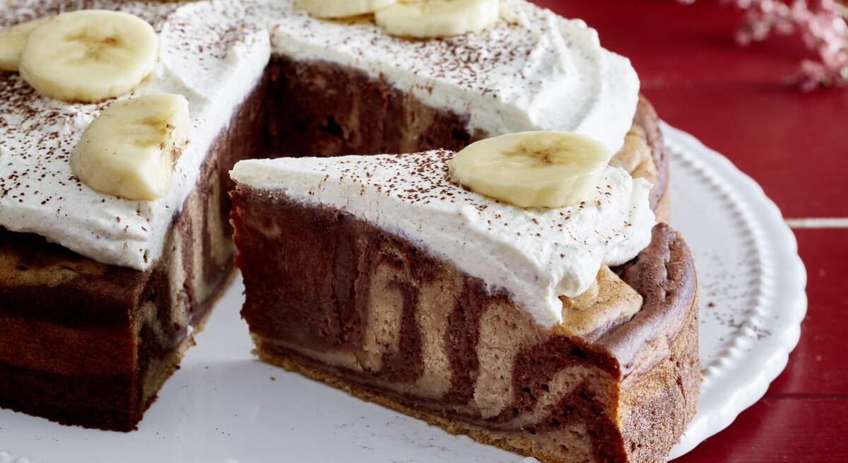 Zebra-Bananen-Kuchen angeschnitten auf einem weißen Teller auf rotem Hintergrund.