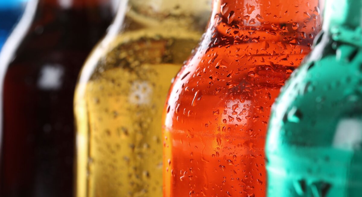Nahaufnahme mehrerer bunter Flaschen mit Kondenswasser, im Vordergrund eine orangefarbene Flasche, dahinter grün und braun.