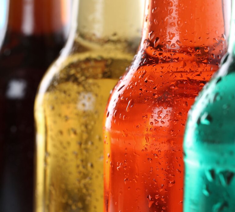 Nahaufnahme mehrerer bunter Flaschen mit Kondenswasser, im Vordergrund eine orangefarbene Flasche, dahinter grün und braun. | © AdobeStock/Markus Mainka