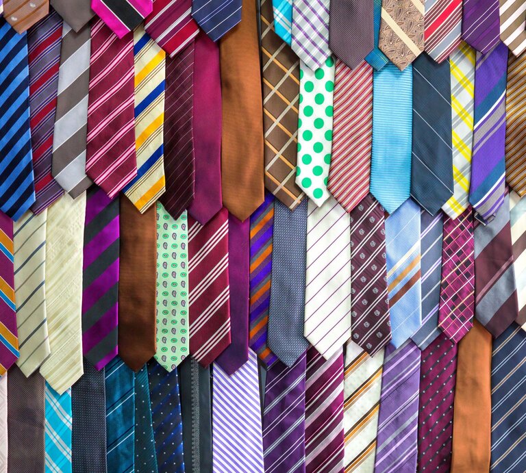 Ein buntes Sortiment an Krawatten in verschiedenen Mustern und Farben hängt geordnet an einer Wand. | © AdobeStock/Nomad_Soul