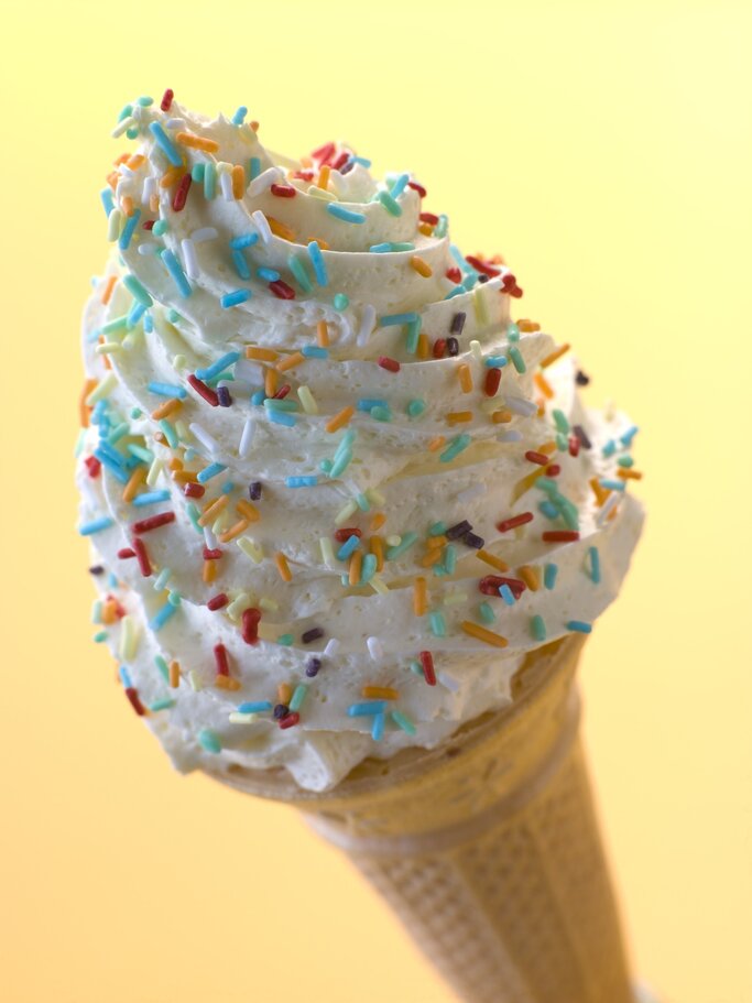 Ein Eis in einer Waffel mit bunter Streusel-Dekoration vor einem hellgelben Hintergrund. | © iStock.com/monkeybusinessimages