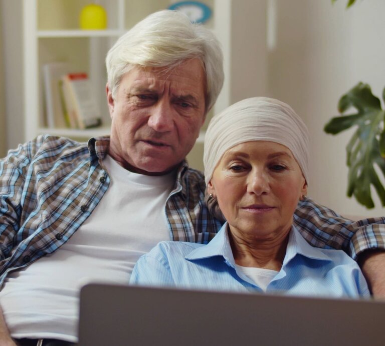 Nachdenkliches Paar in gemütlicher Umgebung, die Frau mit Brustkrebs wirkt ruhig und wird vom Partner gehalten. | © Adobe Stock/ nimito