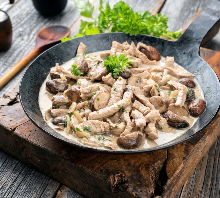 Zürcher Geschnetzeltes in gusseiserner Pfanne auf Holzbrett.  | © Shutterstock/hlphoto
