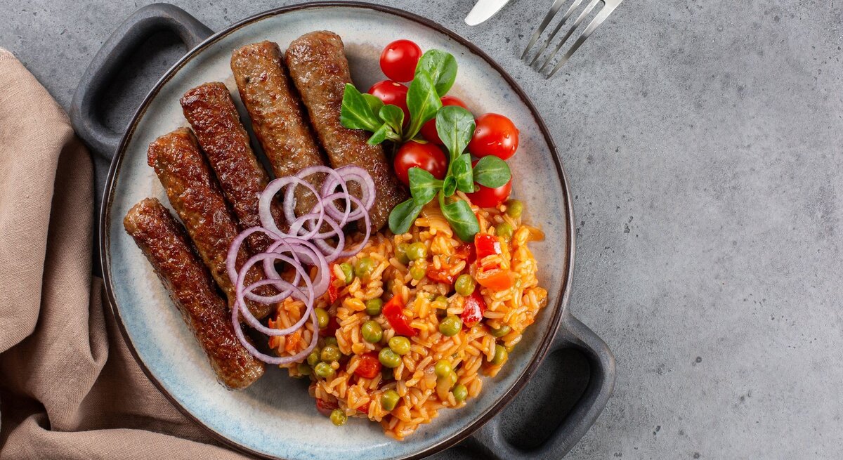 Djuvec-Reis mit Cevapcici auf Teller. 